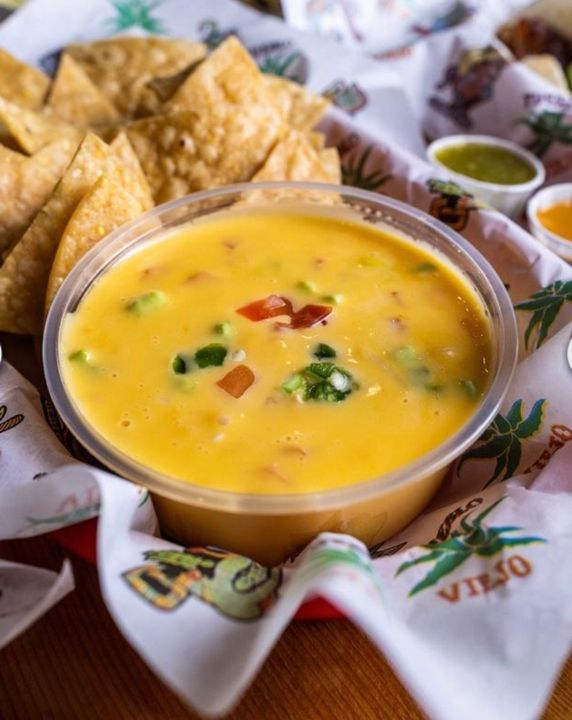 A jar of Chile con Queso with a label and a lid, sitting on a wooden table
