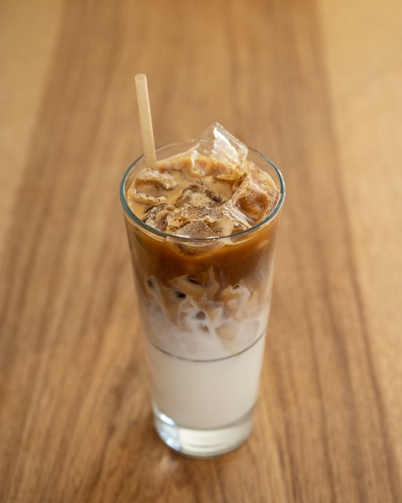 A glass of iced latte with a layer of foam on top