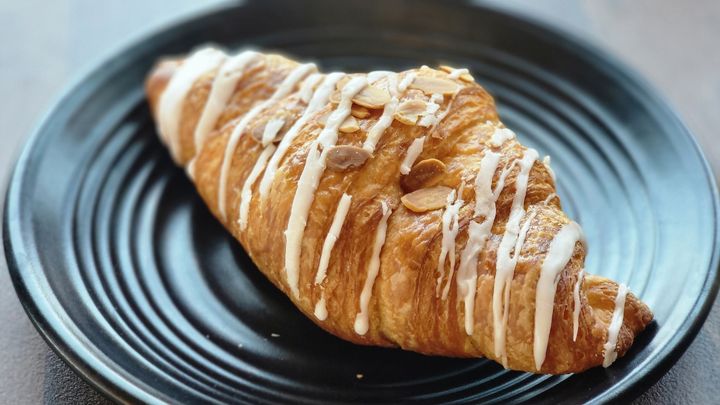 A golden-brown Almond Croissant on a wooden cutting board