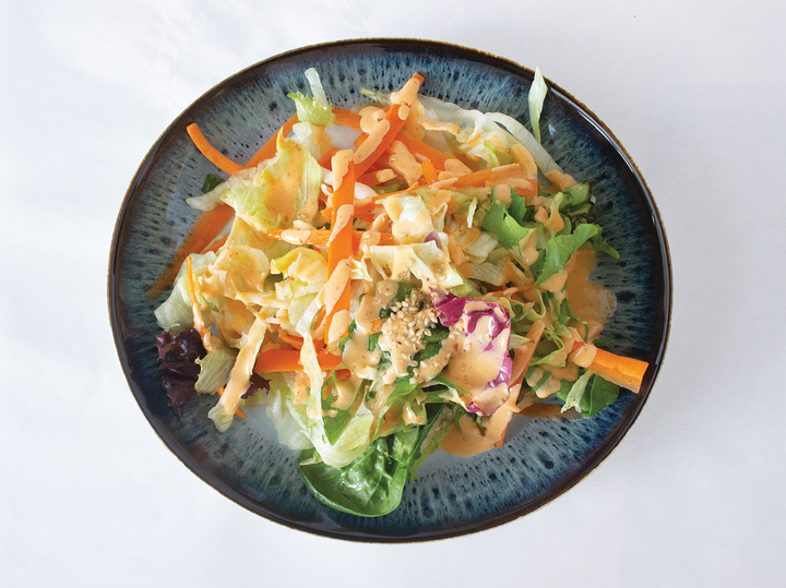 A bowl of mixed greens with vegetables and dressing